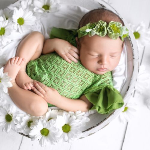 baby wearing green sleeping in a bowl surrounded by white daisies