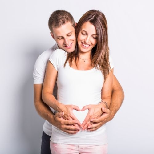 pregnant couple man holding her belly while she makes a heart with her hands 