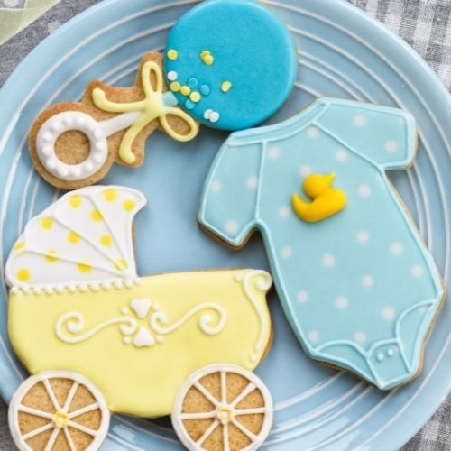 baby shower cookies, blue rattle cookie, blue onesie cookie and a yellow baby pram cookie