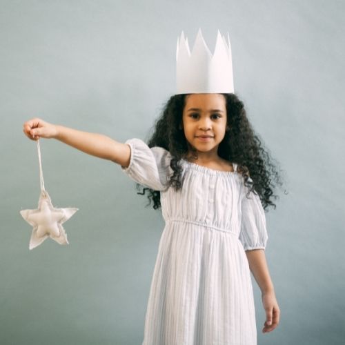 little girl wearing crown with curly hair smiling and holding a star in her right hand. wearing a simple dress