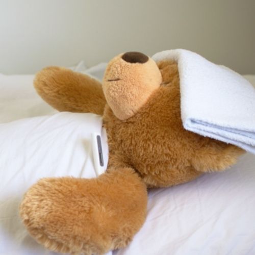 teddy bear laying down with cloth on forehead