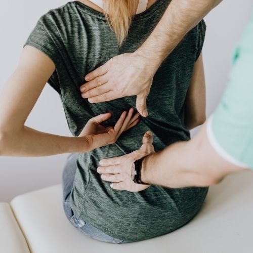 pregnant woman sitting up and holding back while a chiropractor feels 