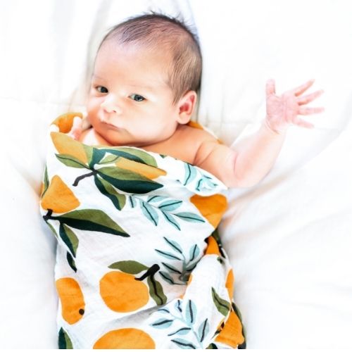 baby swaddled in blanket with oranges on it with left arm out of the swaddle