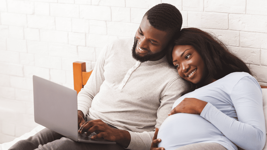 pregnant couple looking at computer smiling and snuggling up together
