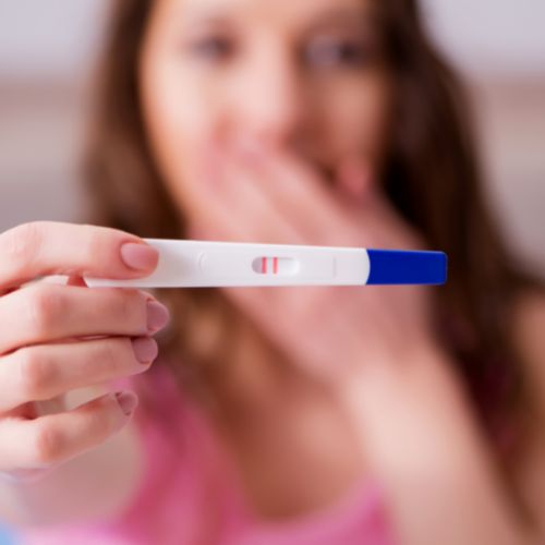 woman in background holding positive pregnancy test