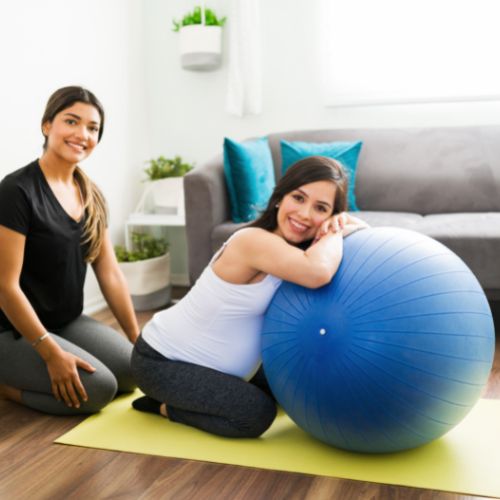 pregnant person leaning against birth ball and a woman sitting behind her