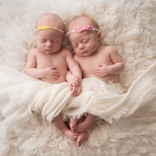twin baby girls with dainty headband on head snuggled next to each other holding hands