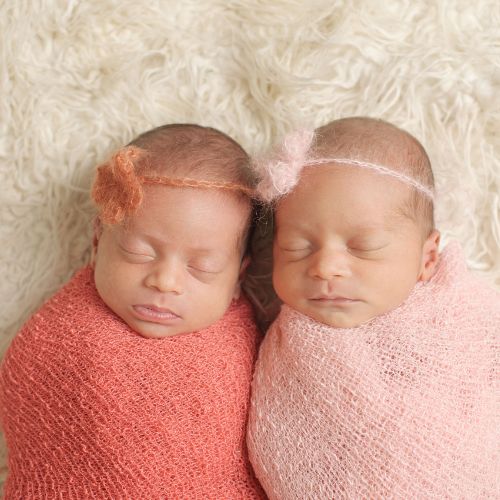 two newborns wearing similar colors of orange and pink swaddled and sleeping next to each other
