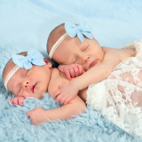 two newborn girls with headband bows on their heads draped in lacy fabric sleeping