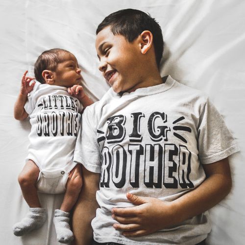newborn baby with older brother wearing matching t-shirts and laying side by side

