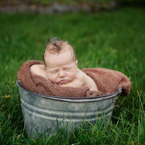 one month old baby sitting outside in a metal bucket with brown blanket inside
