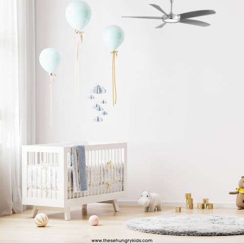 neutral nursery with a fuzzy rug on floor, crib, balloon wall decor, stuffed animals and blocks and a small ceiling fan 