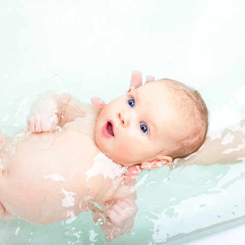 baby looking upwards being held with head above water while laying on back