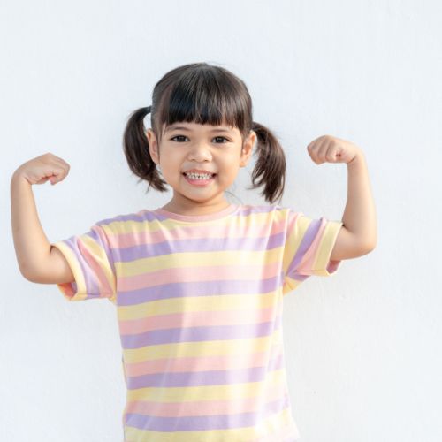 little girl wearing pigtails and smiling making muscles with arms and wearing a striped t-shirt
