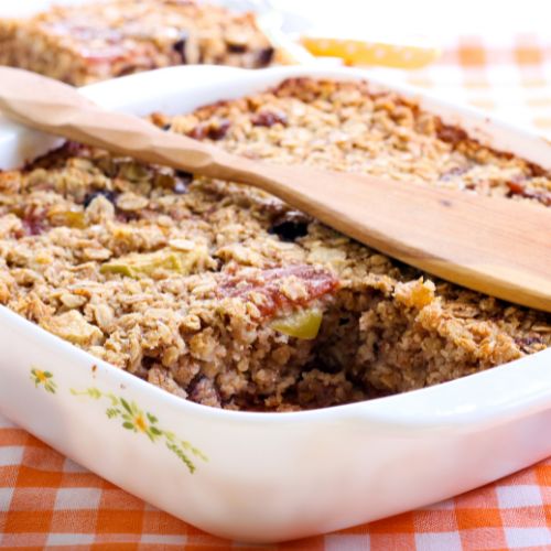 baked oatmeal in a casserole dish with a slice cut out and a spoon laying across
