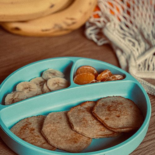 banana pancakes on a kids divider plate with sliced bananas and oranges
