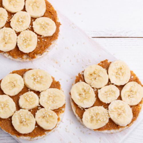 three rice cakes with peanut butter spread over top and sliced bananas topped with sesame seeds on a white plate
