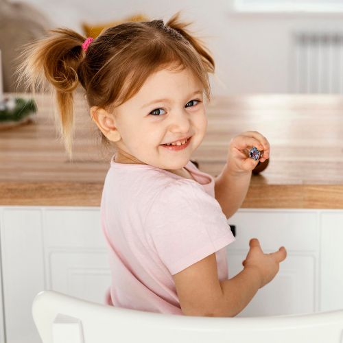 toddler girl with hair in buns sitting at a counter looking over her shoulder and smiling wearing a t-shirt