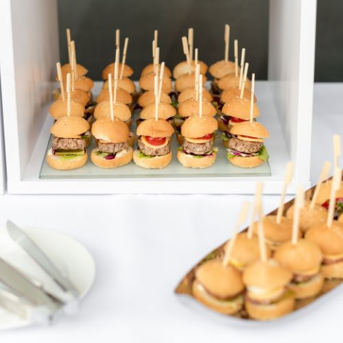on a white backdrop, two trays of mini cheeseburger sliders with a tall skewer through the middle