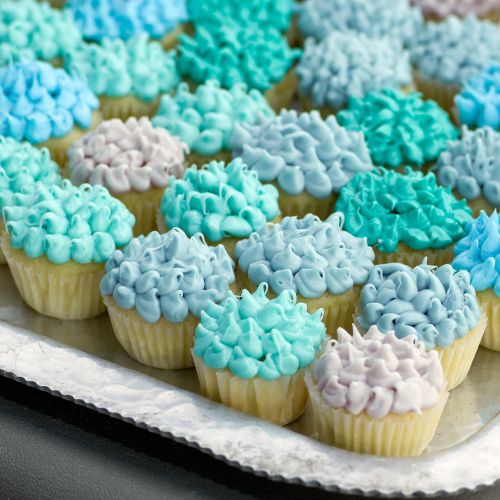 a tray of miniature vanilla cupcakes with frosting piped on in a variety of shades of blue and gray