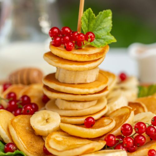 miniature pancakes stacked and skewed with bright red raspberries and banana slices 