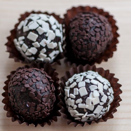 set of four oreo truffles in brown wrapping on a neutral backdrop. two truffles topped with chocolate topping and two with a white chocolate topping