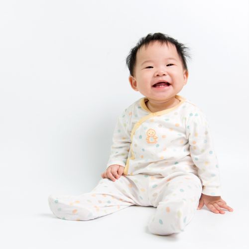 white background with small Asian baby sitting and smiling wearing a white pajama onesie