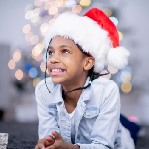 black girl wearing a santa hat and leaning against a countertop smiling and looking upwards 