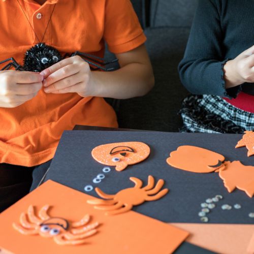 black and orang paper with halloween shaped stickers of pumpkins and spiders with googly eyes and kids hands playing 