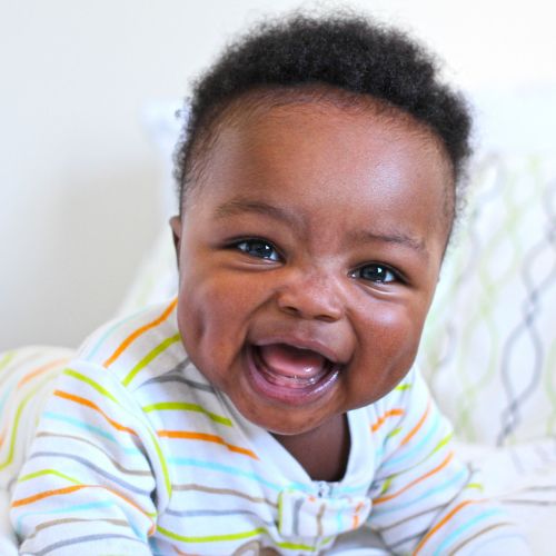 black baby boy smiling wide wearing white pajamas with colorful stripes