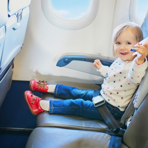 toddler sitting on a plane smiling and holding a small toy 