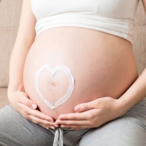 woman sitting holding pregnant belly with lotion drawn in a heart over her belly