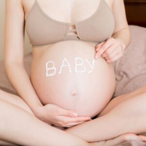 woman sitting holding pregnant belly and with the words "BABY" written in lotion 